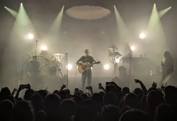Koncertowy wokalista z gitarą, otoczony dymem i światłami. Publiczność wznosi telefony, wołając "nie zapomnij mnie".