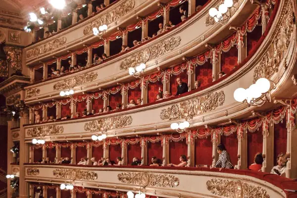 Wnętrze La Scala w Mediolanie, z widownią w lożach, ozdobione złotymi zdobieniami i czerwonymi zasłonami.