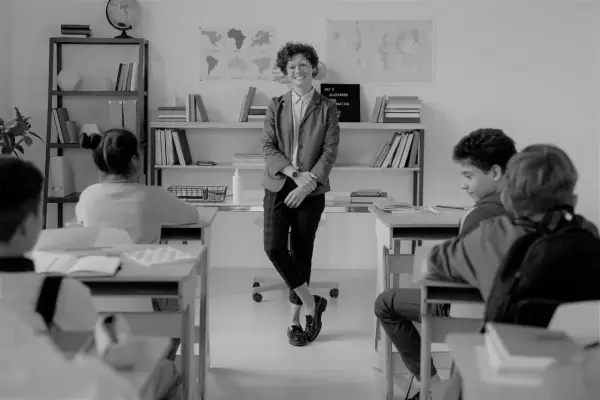 Lehrerin lächelt in einem Klassenzimmer, während Schüler an ihren Tischen sitzen. Eine Szene, die eine gute Klassengemeinschaft widerspiegelt.