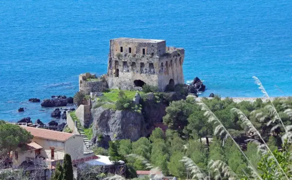 Torre aragonese a picco sul mare, uno dei borghi da visitare in Calabria, con case e vegetazione lussureggiante.