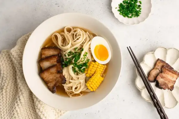 A miseczce aromatyczny shoyu ramen z makaronem, plastrami boczku, jajkiem na pół, kukurydzą i szczypiorkiem.