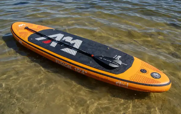Pomarańczowy aquamarina sup z wiosłem leży na płytkiej, przejrzystej wodzie.