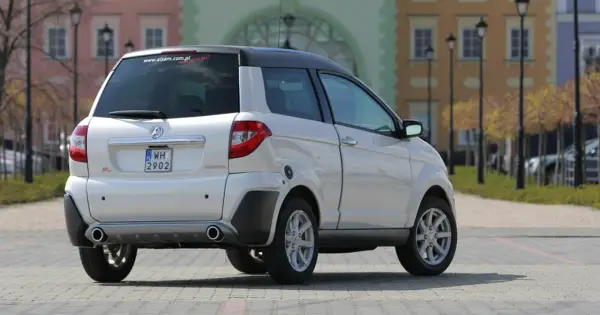 Białe auto Aixam GTR, idealne jako auto bez prawka, parkuje na brukowanym placu przed kolorowymi kamienicami.
