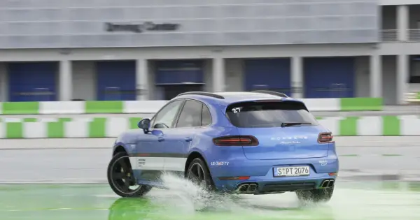 Niebieski Porsche Macan Turbo na mokrym torze Driving Center, rozpryskuje wodę. DSC co to? System stabilizacji toru jazdy.