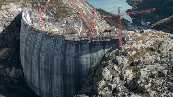 Bau einer gewaltigen Staumauer, die an Pumpspeicherkraftwerke in Deutschland erinnert. Kräne ragen in den Himmel, während die Betonkonstruktion wächst.