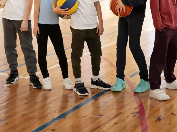 Dzieci na sali gimnastycznej, zastanawiające się, jakie buty na WF do szkoły wybrać. Różne modele sportowego obuwia na drewnianej podłodze.