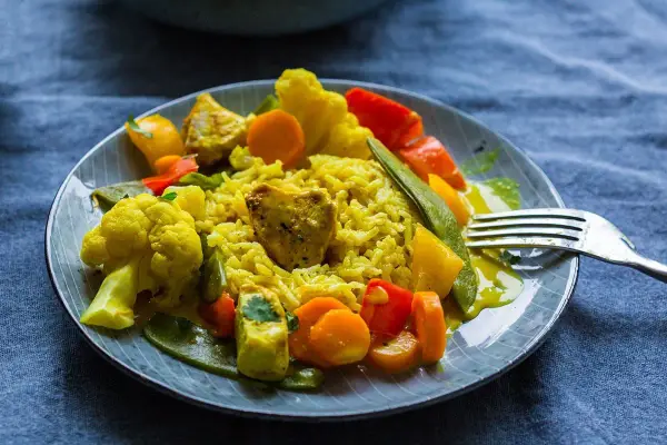 Ein Teller mit gelbem Reis, Blumenkohl, Karotten, Paprika und Erbsen. Ein köstliches Curry Geschnetzeltes, bereit zum Genießen.