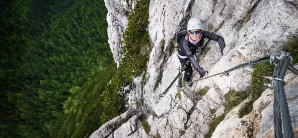 Kobieta wspina się po via ferrata w Dolomitach, z widokiem na gęsty las poniżej.