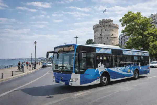 Autobus miejski z motywem fal i mapy Grecji przejeżdża obok Białej Wieży, ikony Salonik.