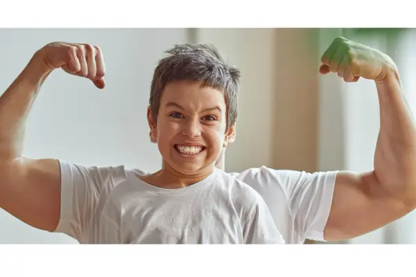 Chłopiec z miną jak po **buncie 5 latka** pokazuje swoje małe bicepsy, podczas gdy za nim widać potężne ramiona taty.