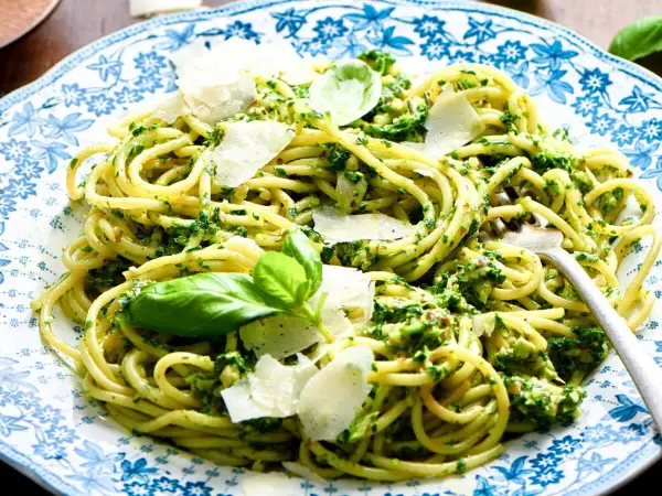 Pâtes au pesto, une recette italienne savoureuse avec des copeaux de parmesan et des feuilles de basilic frais.