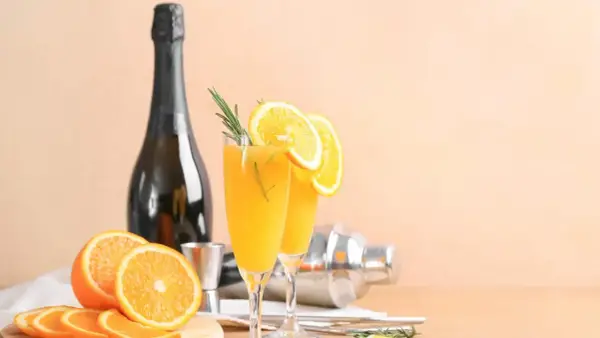 Dwa kieliszki z pomarańczowym drinkiem, ozdobione plasterkami pomarańczy i rozmarynem. Obok butelka, shaker i świeże pomarańcze. Wódka łza pszenicy idealnie pasuje do takiego orzeźwienia.