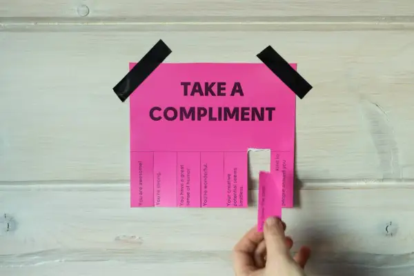 Różowa kartka z napisem "TAKE A COMPLIMENT" i odrywanymi kuponami z pochwałami. Daje to pomysł na inteligentne odpowiedzi na komplementy.