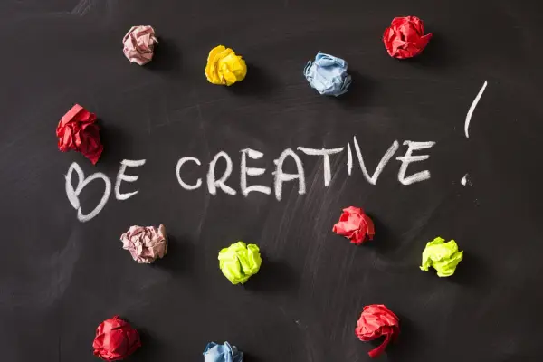 Kolorowe kulki papieru na czarnej tablicy, z napisem "BE CREATIVE!". To inspiracja, jak oszukać system binarny, myśląc nieszablonowo.