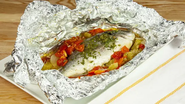 Orata al cartoccio con pomodorini e verdure, cotta al forno e servita in un foglio d'alluminio aperto.