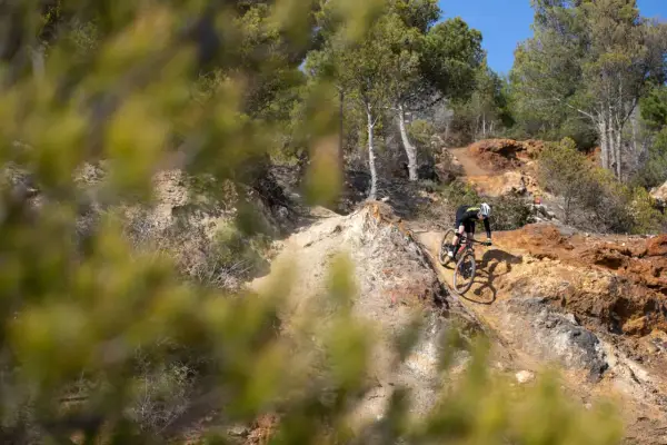 Ciclista su un sentiero sterrato, tra rocce e pini, esplora i percorsi MTB Toscana.