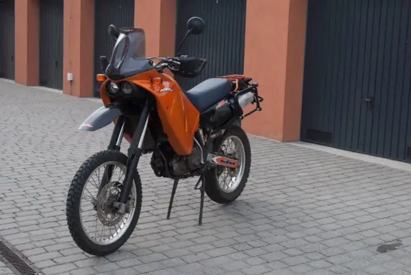 Pomarańczowy motocykl KTM 640 Adventure stoi na brukowanym podjeździe przed garażami.