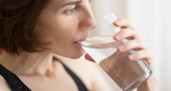 Kvinna dricker vatten för att lindra muntorrhet, en potentiell biverkning av cancerbehandling.