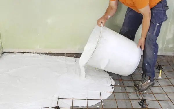 En person häller ut ett vitt material ur en stor hink över ett armeringsnät. Inspiration för betonggolv.