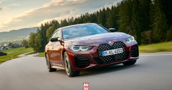 Czerwone BMW G26 z charakterystycznym grillem pędzi po krętej drodze wśród zielonych wzgórz i lasów.