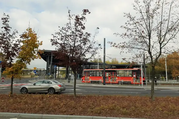 Srebrny samochód i czerwony tramwaj na przystanku, otoczone jesiennymi drzewami. Non stop big single.