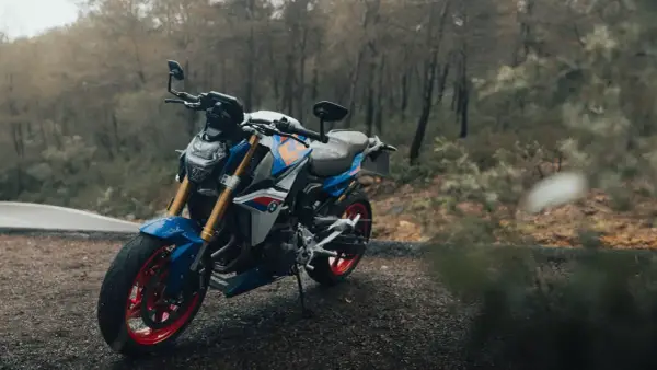 Niebiesko-biały motocykl BMW F900R z czerwonymi felgami na tle jesiennego lasu.