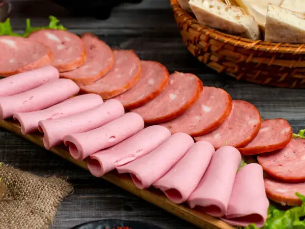 Na desce ułożone są różowe parówki i plastry wędliny. Zastanawiasz się, jakie wędliny są najzdrowsze?