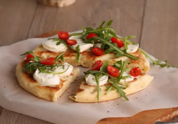 Pyszna focaccia z mozzarellą, pomidorkami koktajlowymi i rukolą, podana na papierze do pieczenia.