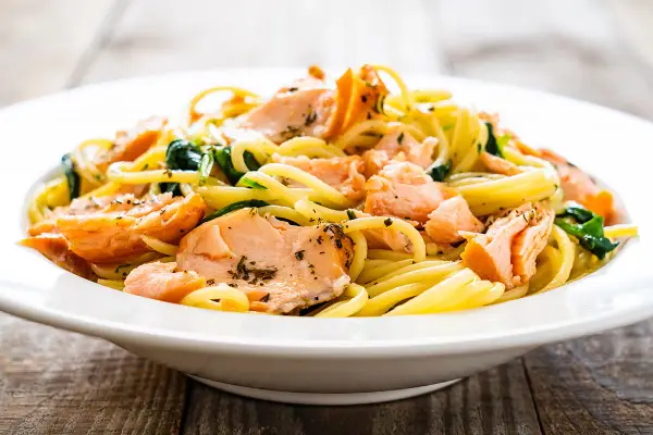 Deliciosa pasta con salmón desmenuzado y espinacas, servida en un plato blanco sobre una mesa de madera.