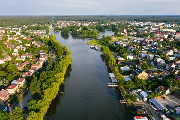 Malowniczy widok na Augustów i jego atrakcje: rzeka, zielone brzegi, domy i las w tle.