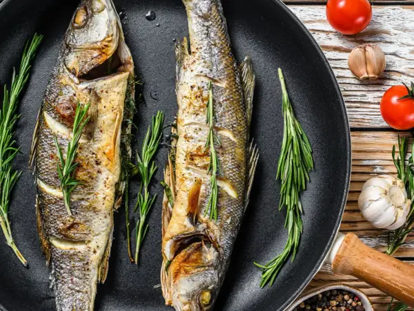 Due branzini dorati in padella, profumati al rosmarino, pronti per essere gustati.
