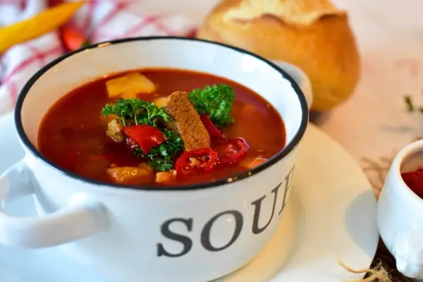 Aromatyczna zupa gulaszowa w białej misce z napisem "SOUP", ozdobiona natką pietruszki i papryką. Idealna na chłodne dni, to jedne z tych **dobrych zup domowych**.