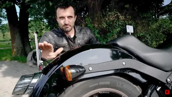 Mężczyzna pokazuje mocowanie tablicy rejestracyjnej motocykl, omawiając przepisy.