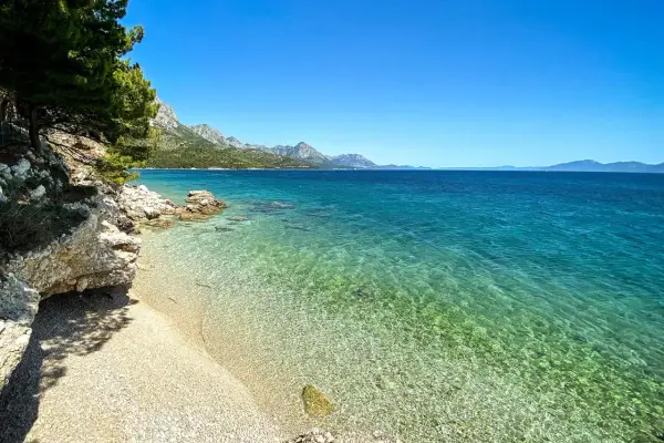 Idealne miejsce na camping w Chorwacji: kamienista plaża, turkusowa woda i góry w tle.