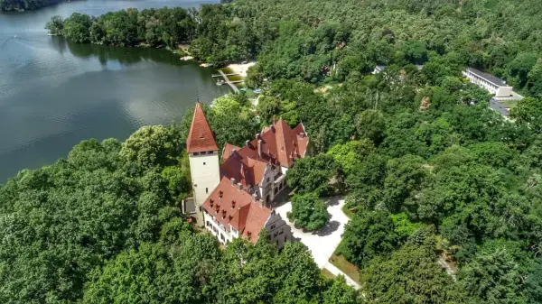 Zamek w Lubniewicach, otoczony bujną zielenią, malowniczo położony nad jeziorem.