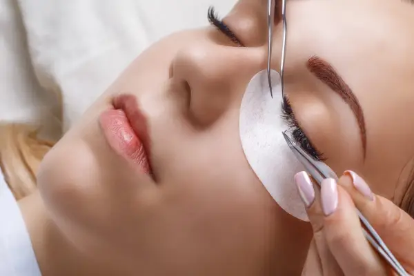 Une esthéticienne utilise des pinces pour appliquer des extensions de cils, une étape clé pour savoir comment coiffer ses sourcils et sublimer le regard.