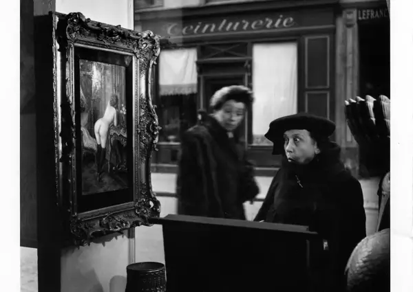 Una donna guarda un quadro in una vetrina, un'altra figura sfocata sullo sfondo. Robert Doisneau foto.