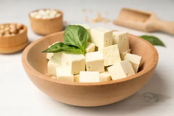 Kostki tofu w drewnianej misce z bazylią. Czy tofu można jeść na surowo? Tak, to idealny składnik do sałatek i przekąsek.