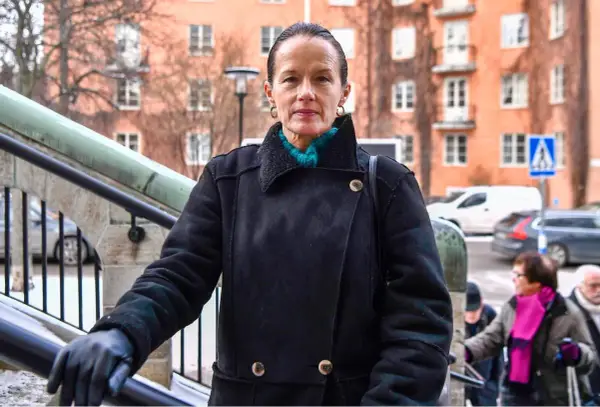 Malin Berghagen, trots att hon verkar sjuk, går uppför en trappa i en svart kappa.