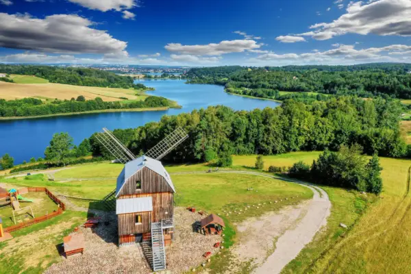 Drewniany wiatrak nad jeziorem, otoczony zielenią. To jedno z magicznych miejsc na Kaszubach, gdzie czas płynie wolniej.