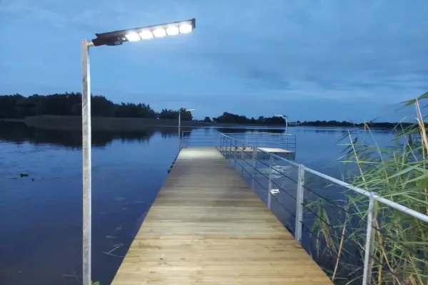 Drewniany pomost nad jeziorem, oświetlony lampami, zachęca do spaceru. Czy pomost nad jeziorem może być prywatny? Ten wygląda na dostępny dla wszystkich.
