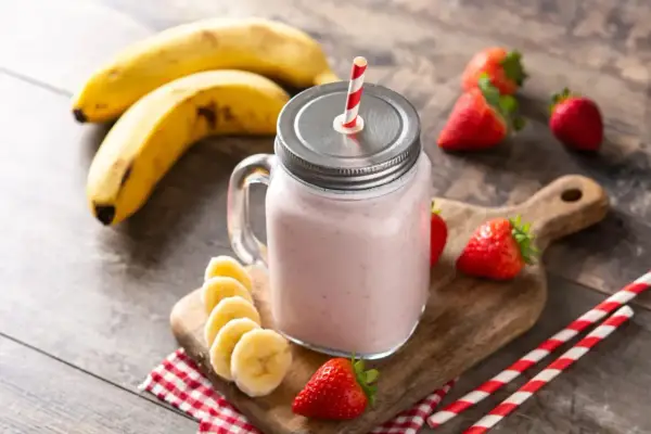 Un délicieux smoothie fraise banane dans un bocal en verre, garni de fruits frais et de pailles rayées.