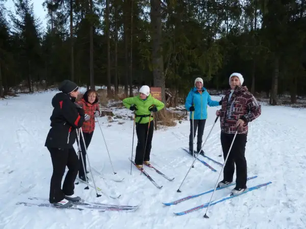 Grupa osób w strojach na narty biegowe przygotowuje się do jazdy w lesie.