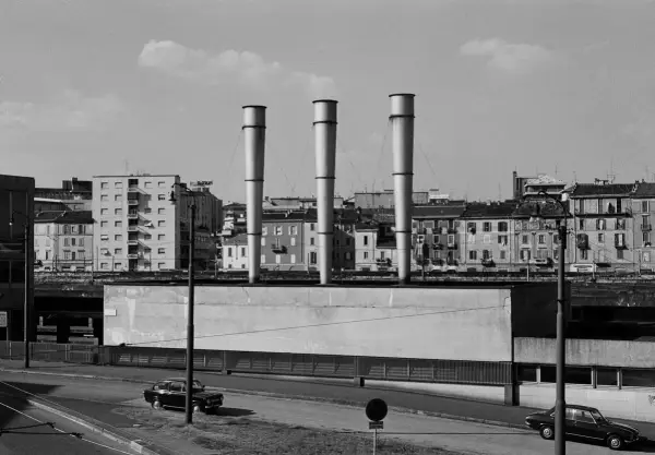 Gabriele Basilico foto: tre ciminiere svettano su un paesaggio urbano con palazzi e auto.