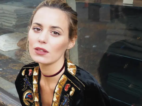 Claudia Ortiz Domecq, con un choker de terciopelo y chaqueta bordada, posa con mirada intensa frente a un escaparate.
