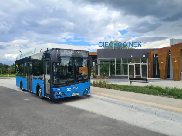 Niebieski autobus ekologiczny z napisem "Ciechocinek Dworzec" czeka na pasażerów. W tle nowoczesny budynek dworca z napisem "Ciechocinek".