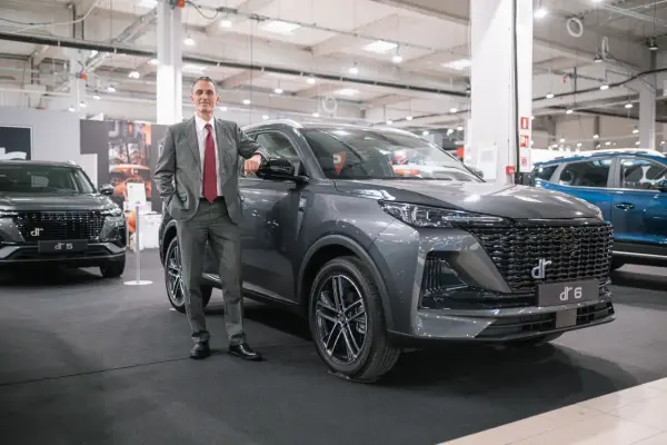 Mężczyzna w garniturze opiera się o szare auto DR 6. Obok stoi DR 5.