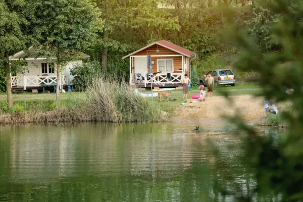 Rodzina odpoczywa nad jeziorem w malowniczym miejscu. Dzieci pluskają się w wodzie, a dorośli relaksują się na plaży przy domkach kempingowych. To idealne miejsce na rodzinne wakacje, prawdziwa **camping forteca** spokoju i radości.