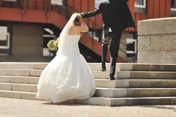 Un couple s'enfuit sur des escaliers après leur cérémonie de mariage. La mariée porte une robe blanche et un voile, tenant un bouquet.