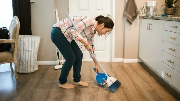 Mujer barriendo el suelo con escoba y recogedor, aplicando trucos de limpieza para mantener el hogar impecable.